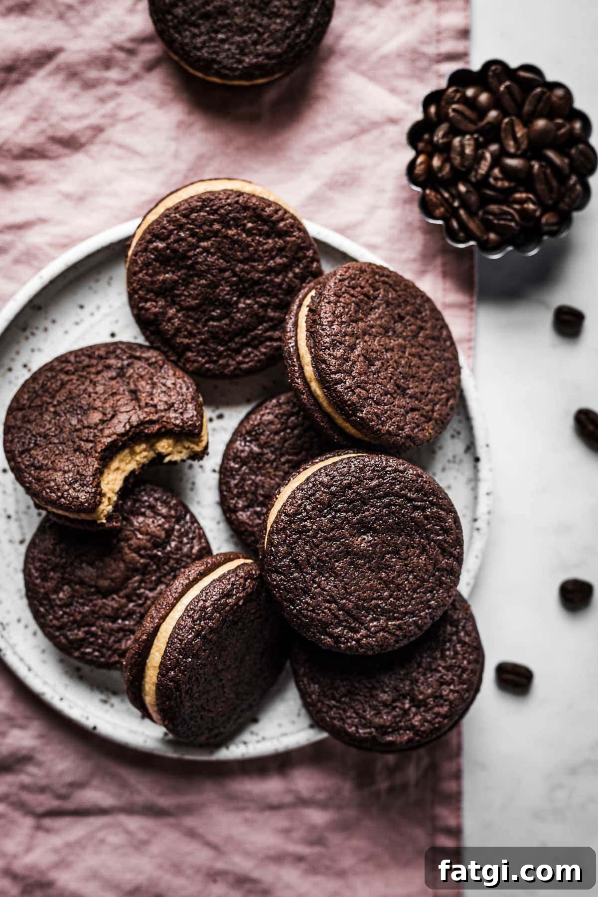Sandwich cookies stacked on a speckled plate. One cookie has a bite missing.