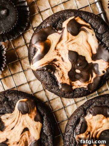 Three chocolate peanut butter cup cookies on a vintage metal cooling rack surrounded by wrapped and unwrapped chocolate peanut butter cups.