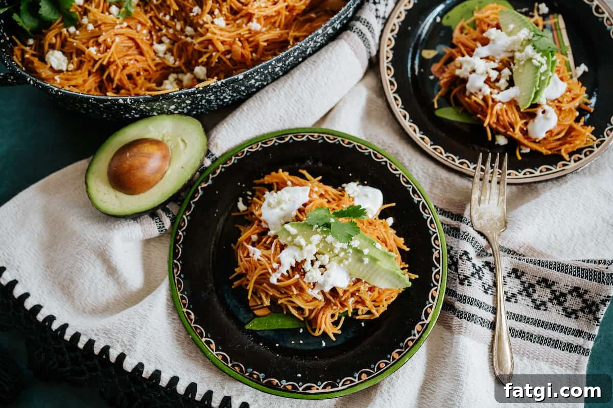 overhead shot of two plates of Mexican fideo seco pasta with avocado, crema, cilantro, and queso fresco. 