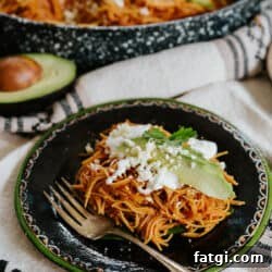 45 degree angle shot of a black plate with a green rim filled with a serving of fideo seco topped with avocado slices, a drizzle of crema, and a sprinkle of queso fresco.