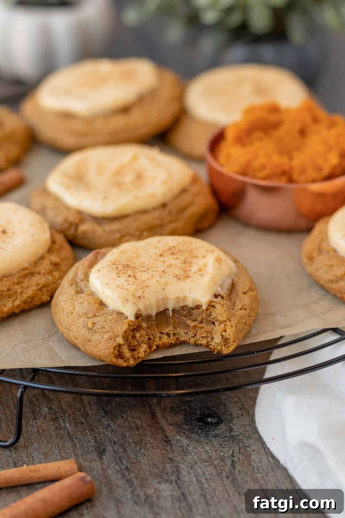 Creamy Pumpkin Cheesecake Cookies 2 pumpkin cheesecake cookies sitting on a black wire cooling rack with measuring cup of pumpkin next to them