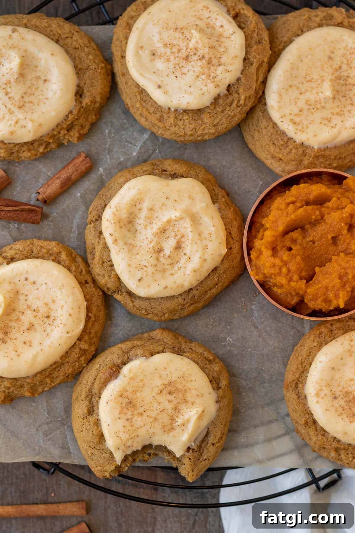 Creamy Pumpkin Cheesecake Cookies 3 pumpkin cheesecake cookies on a cooling rack on a wood background with pumpkin puree in a measuring cup