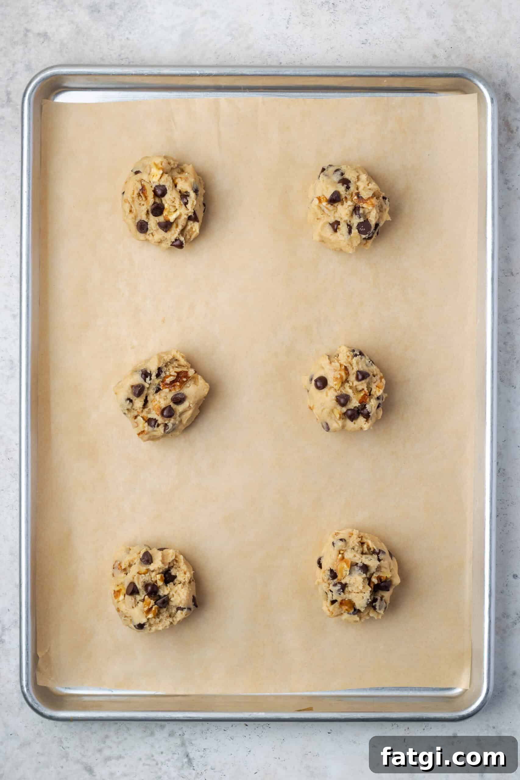 Six balls of walnut chocolate chip cookie dough on a baking sheet.