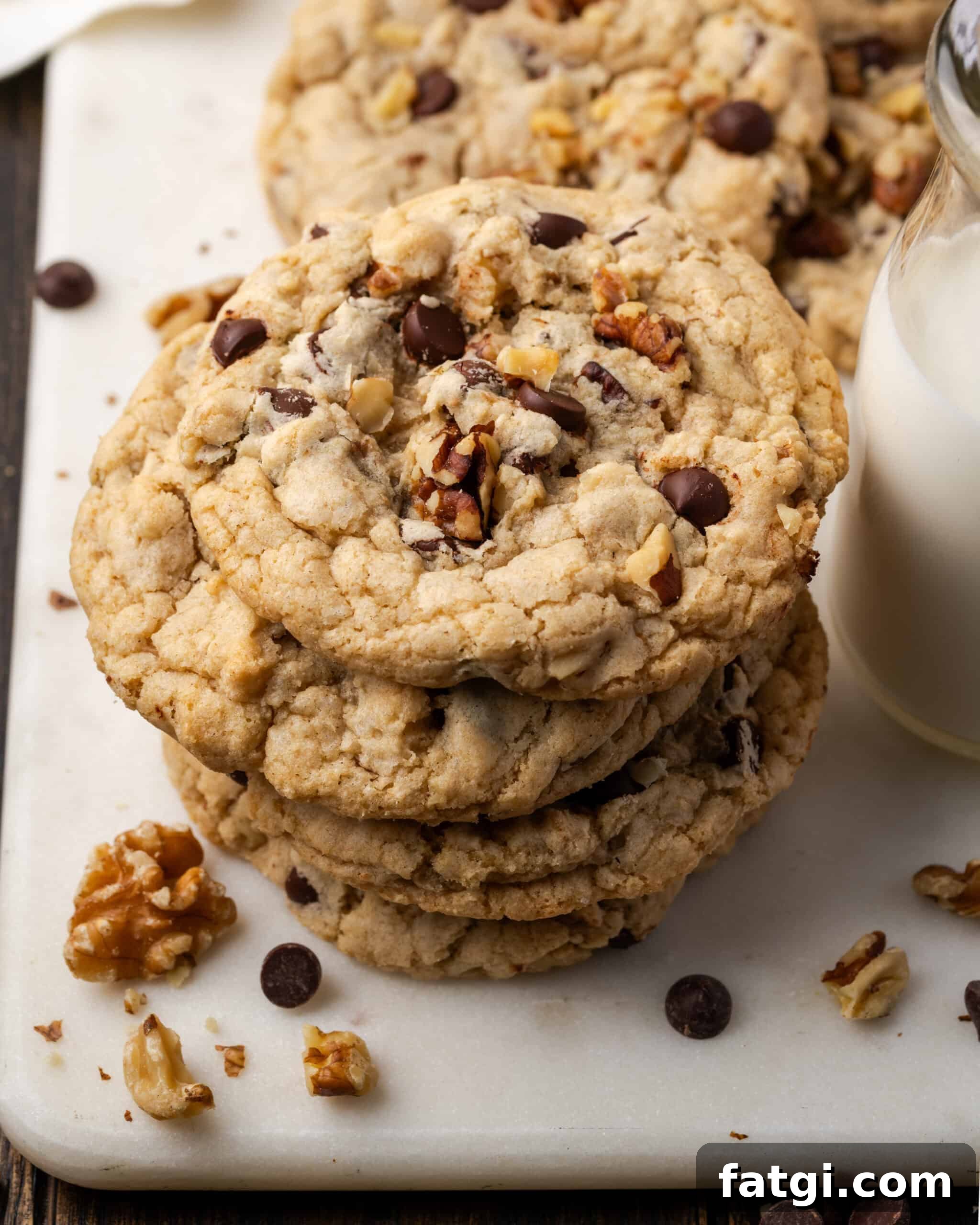 A stack of gluten free walnut chocolate chip cookies sitting on a cutting board next to a jar of milk.