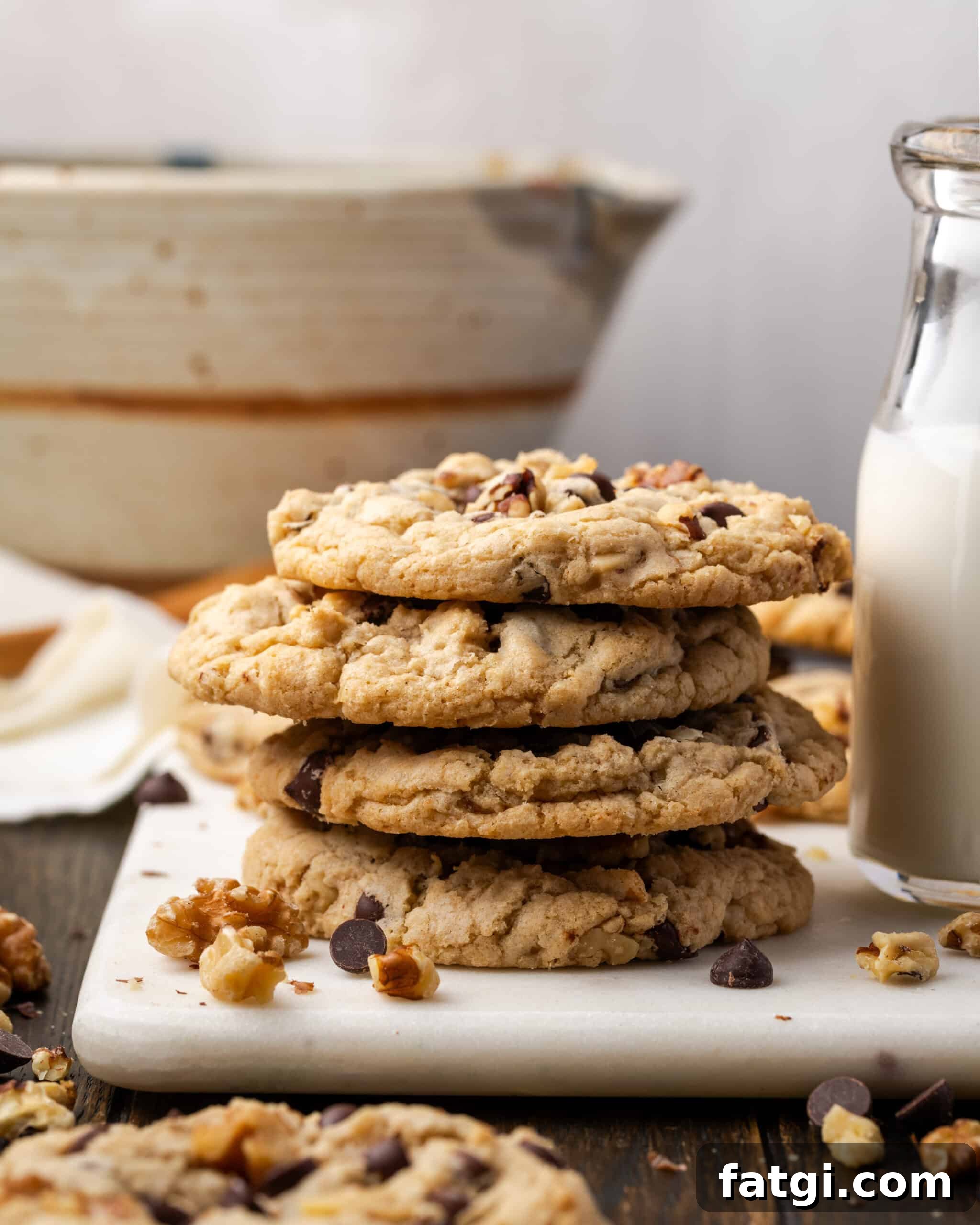 A stack of four walnut chocolate chip cookies sitting next to a jar of milk. 