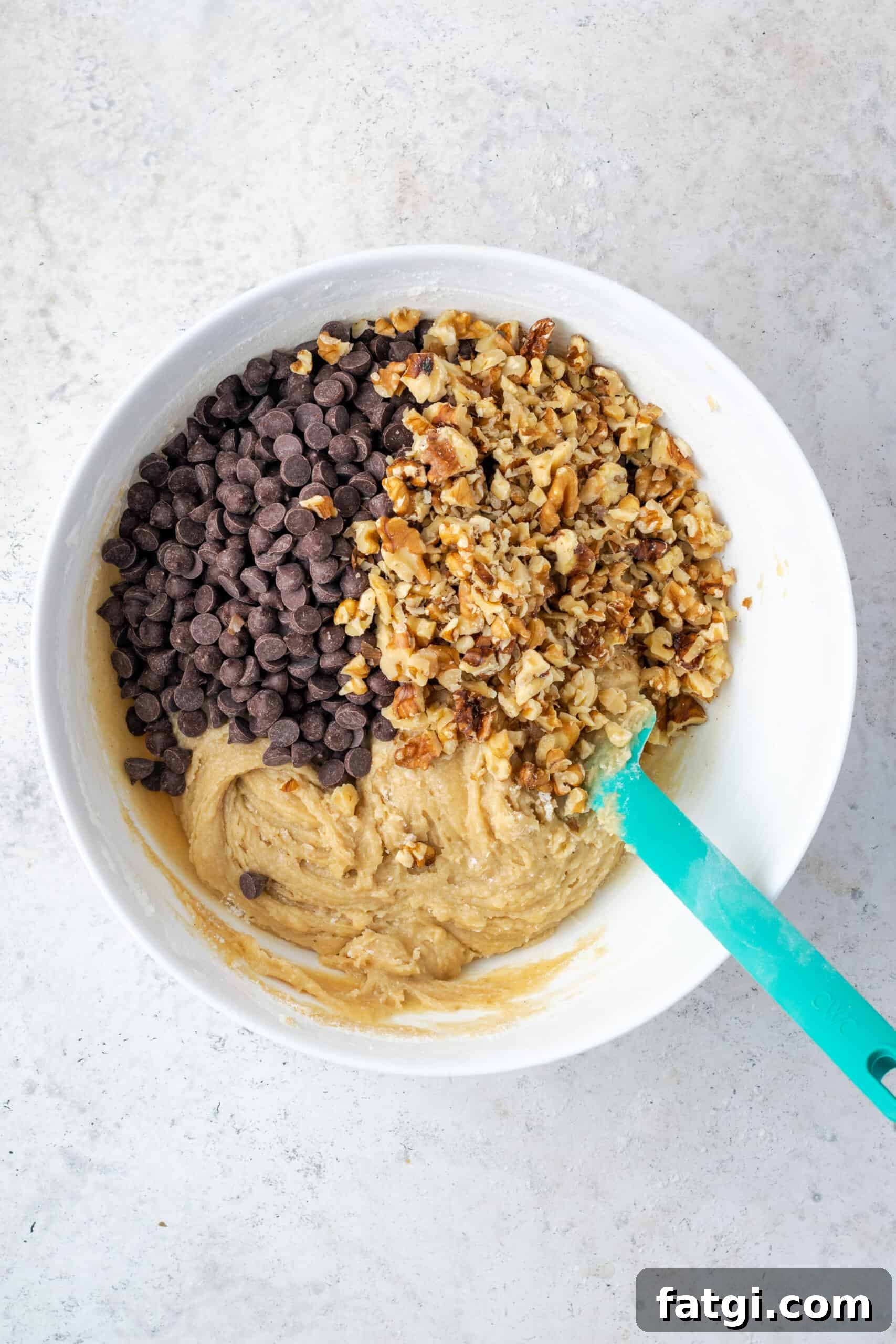 Chocolate chips and walnuts being folded into the cookie dough.