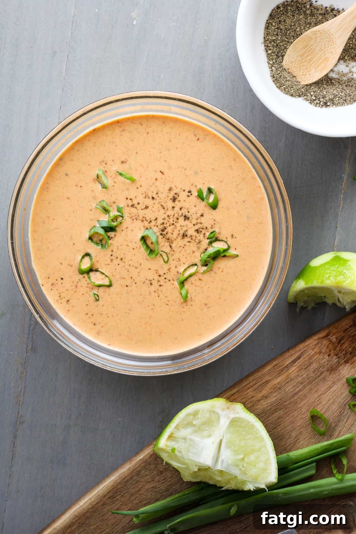 A small bowl of creamy chipotle lime sauce with a cutting board off center holding a lime and scallions.