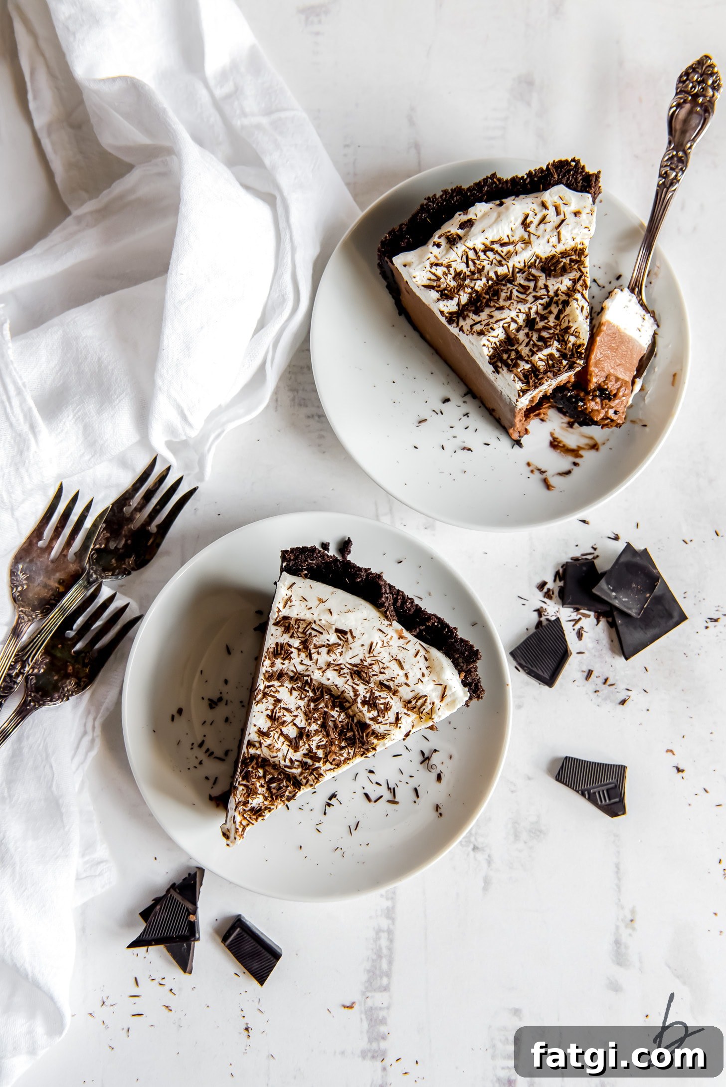 two plates each with a slice of chocolate cream pie with whipped cream and chocolate shavings