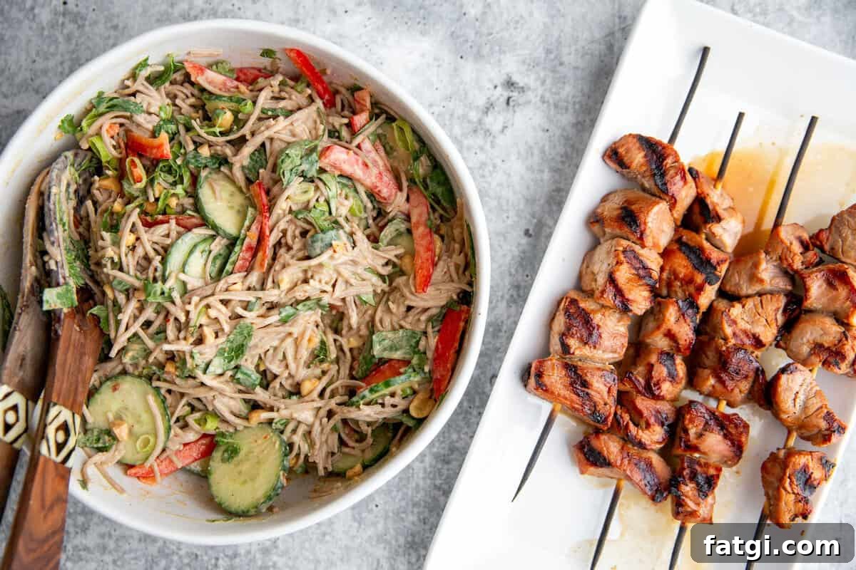 Juicy Marinated Pork Kebabs with Peanut Noodle Salad 3 A soba noodle salad tossed in peanut dressing next to plated grilled pork kebabs on wooden skewers