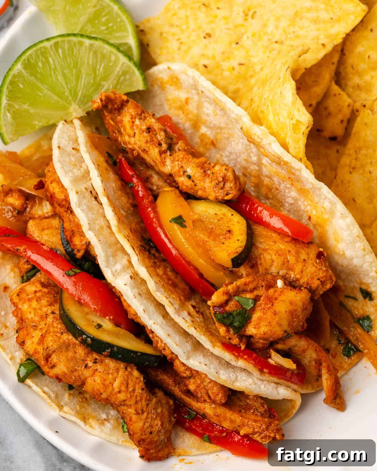 Sheet Pan Chicken Fajitas with Peppers and Onions 9 Two corn tortillas filled with chicken fajitas served on a plate with corn chips.