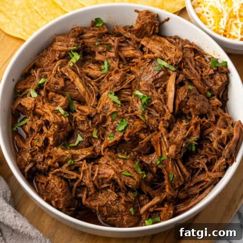 A bowl filled with beef barbacoa sitting on a wooden cutting board.