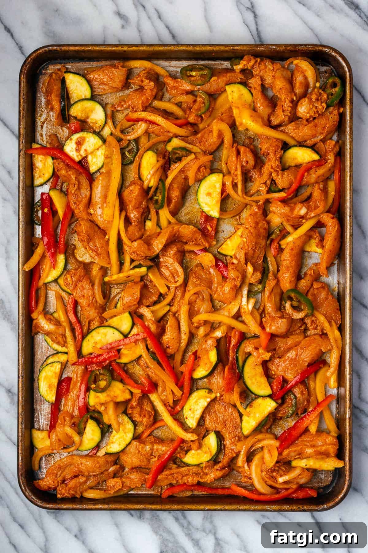 Sheet Pan Chicken Fajitas with Peppers and Onions 7 Uncooked chicken fajitas spread on a large sheet pan.