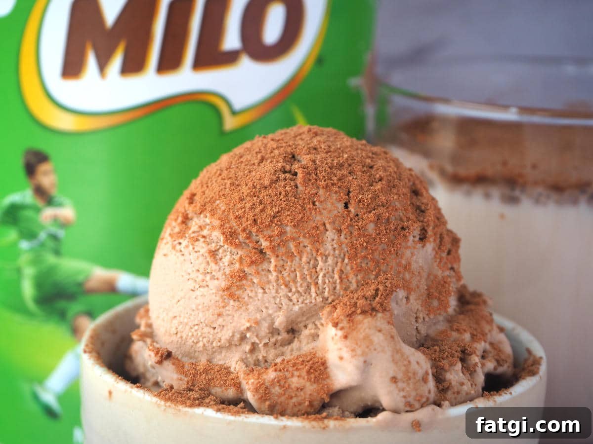 Close up scoop Milo ice cream sprinkled with Milo, in a small bowl, with Milo tin and glass of Milo in the background.