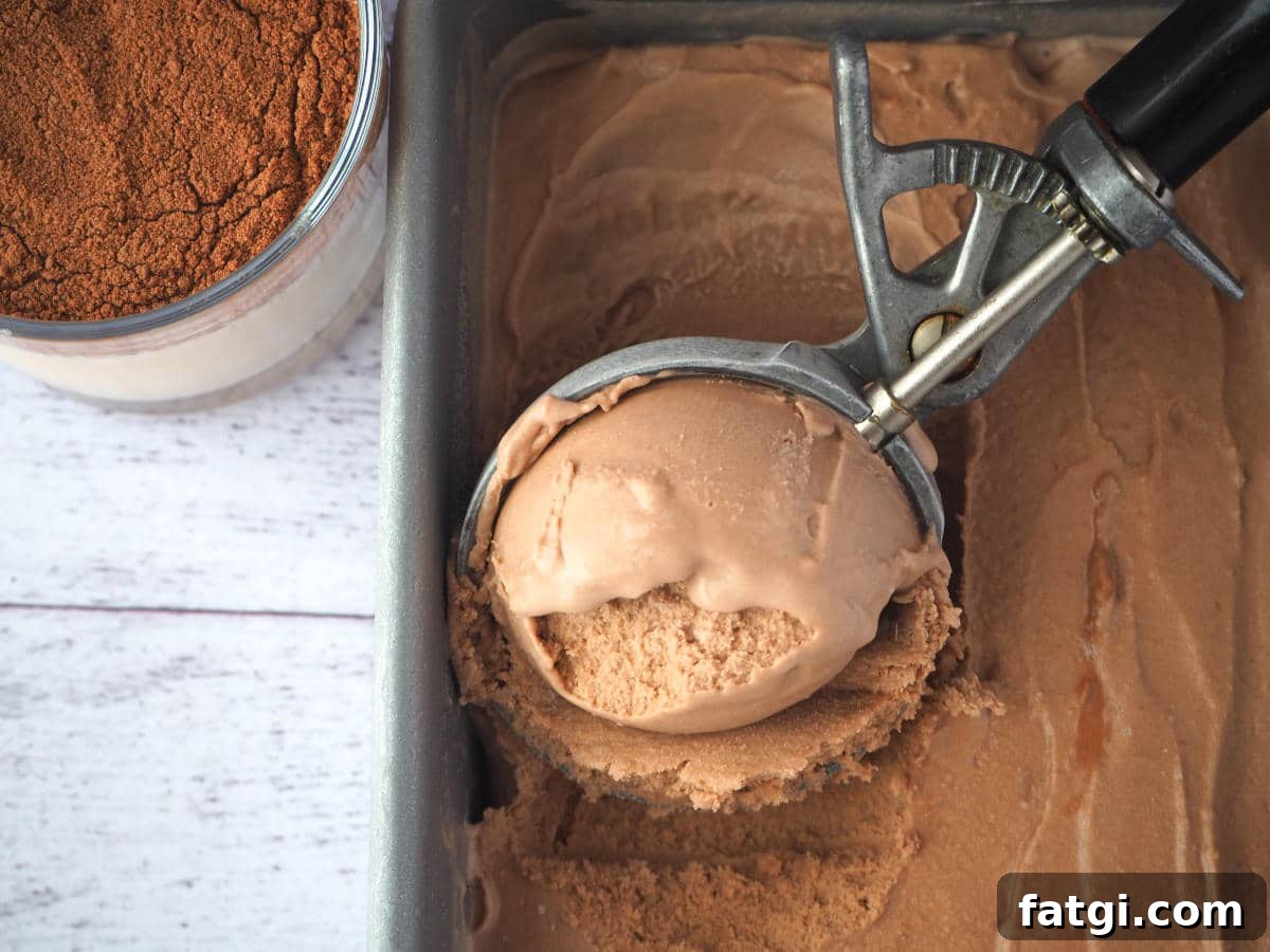 Top down view scooping Milo ice cream in a pan with vintage ice cream scoop, with glass of Milo on the side.