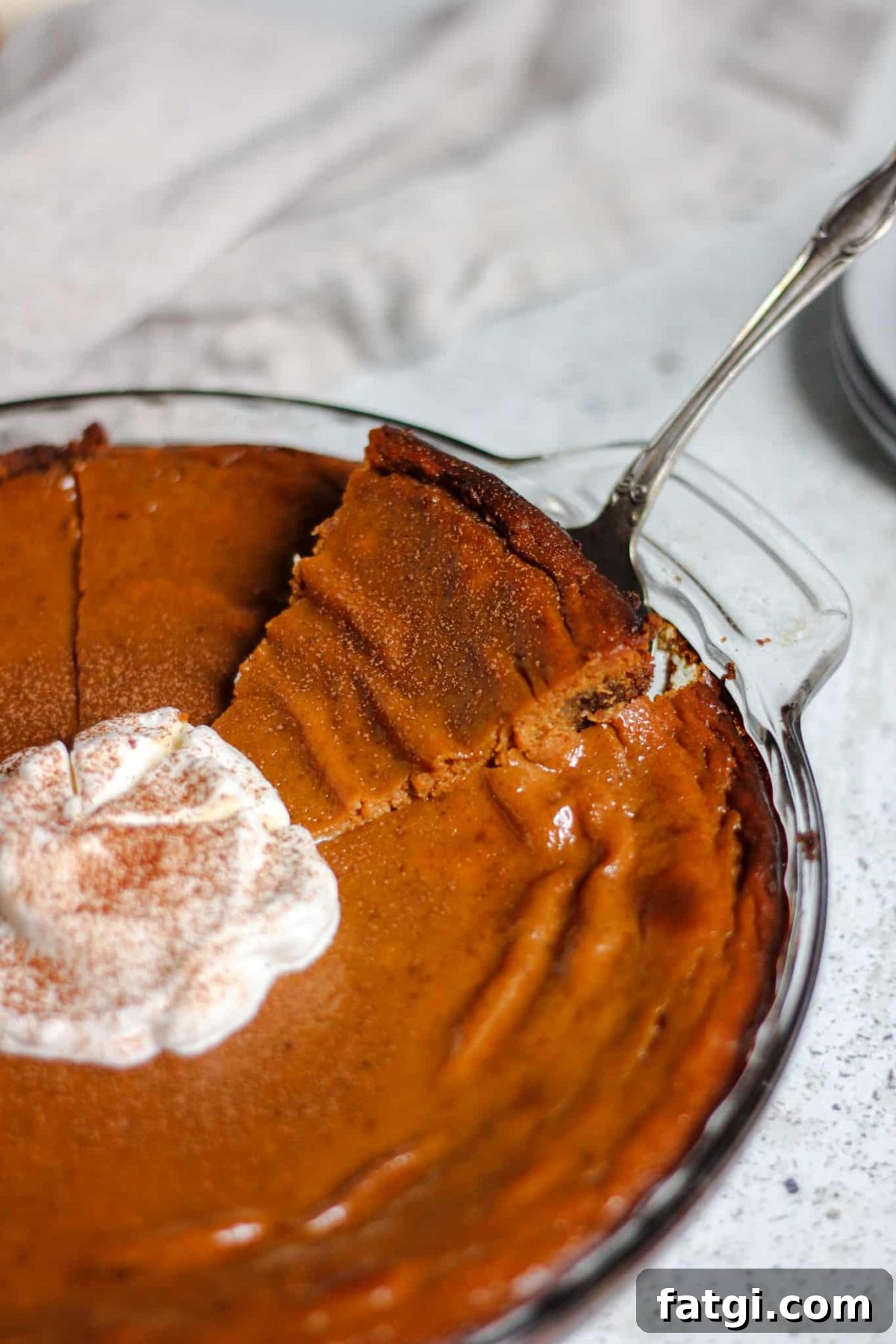 rich pumpkin pie with gingersnap crust serving a slice of pumpkin pie from a glass dish