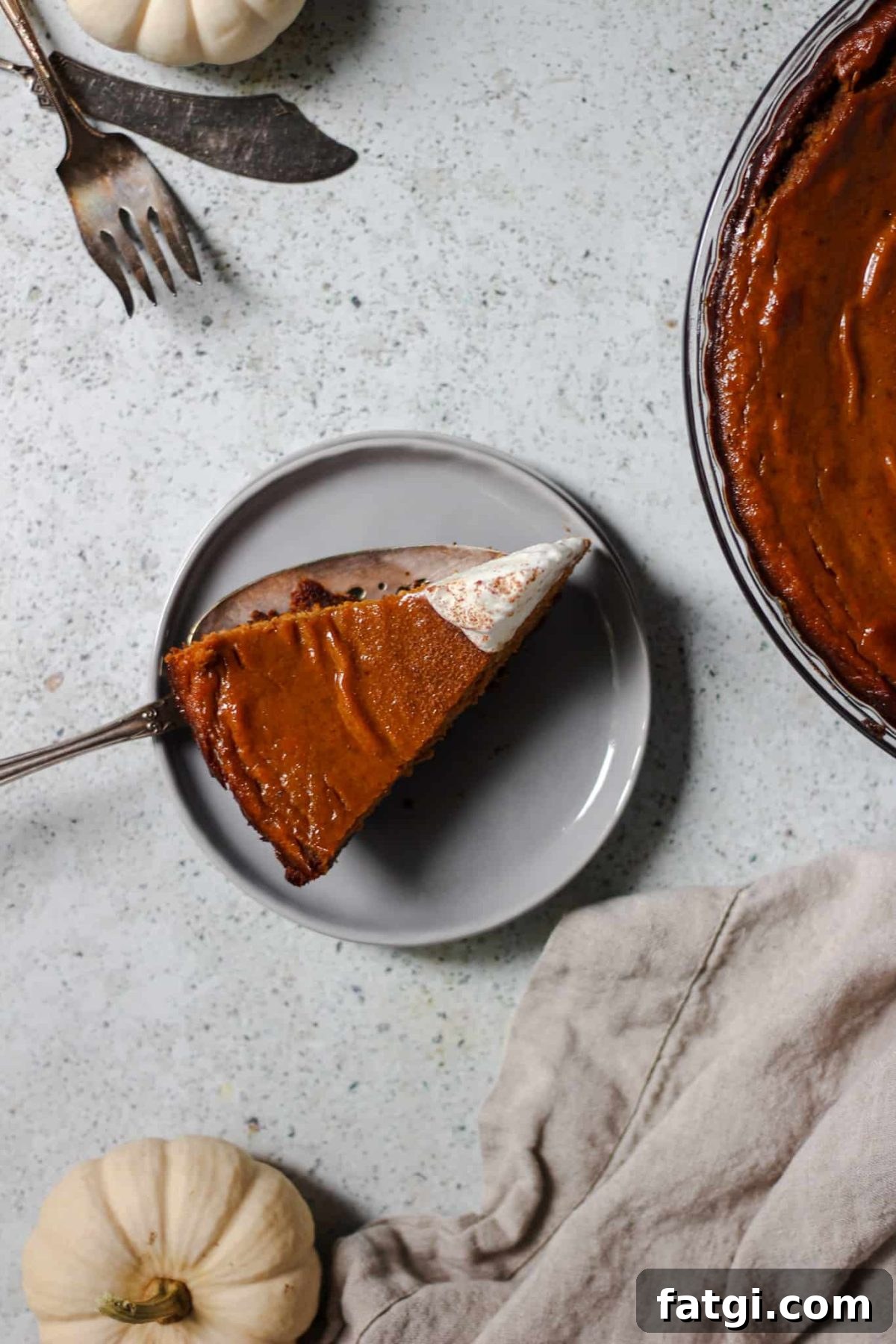 pumpkin pie with gingersnap cookie crust flatlay photo of a slice of fall pie with a linen, silverware and a small white pumpkin
