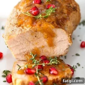 Balsamic Apple Pork Tenderloin garnished with pomegranate and thyme on a white plate