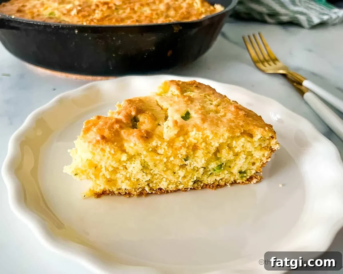 Jiffy Mix Jalapeno Cheddar Cornbread Recipe 7 a white plate with a slice of jalapeno cornbread with a skillet with cornbread, bread knife, fork, and a striped cloth in the background.