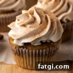 Snickerdoodle cupcakes topped with swirls of cinnamon buttercream frosting on a wooden cutting board.