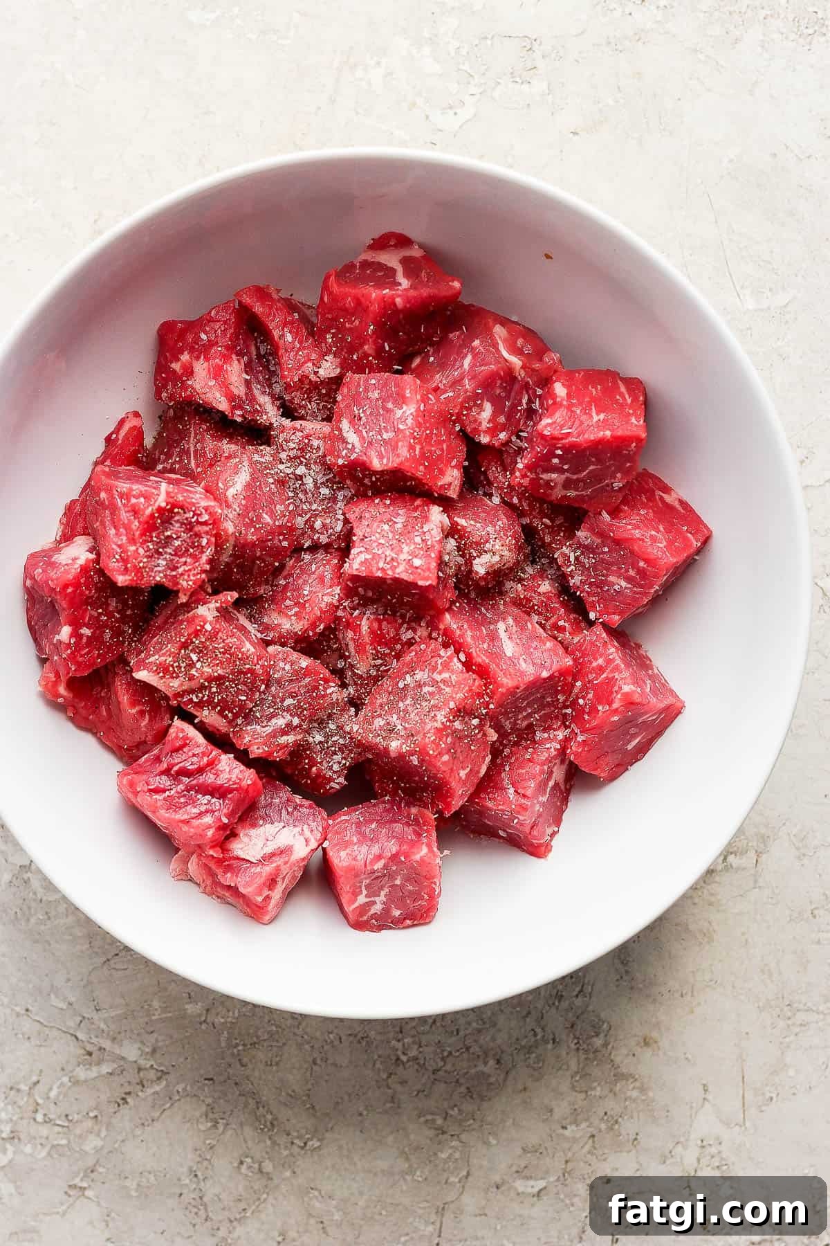 Garlic Butter Steak Bites Recipe 4 Raw steak bites in a white bowl with salt and pepper.