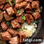 Garlic Butter Steak Bites Recipe 10 Top down shot of a cast iron skillet filled with garlic butter steak bites with fresh parsley as garnish.