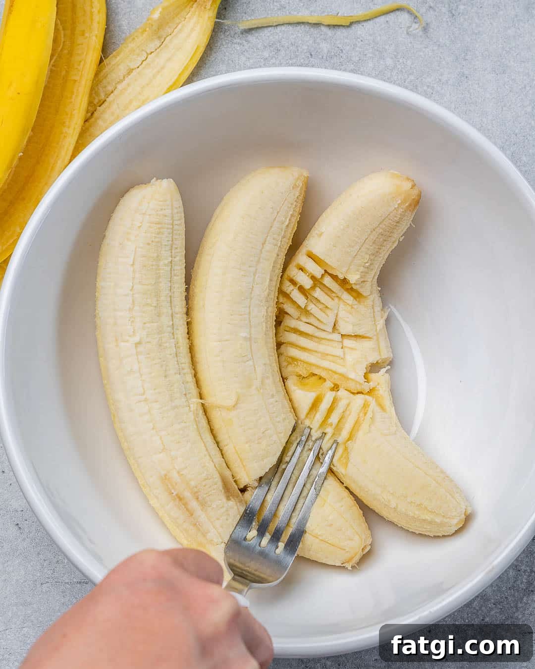 Fork mashing ripe bananas in white bowl