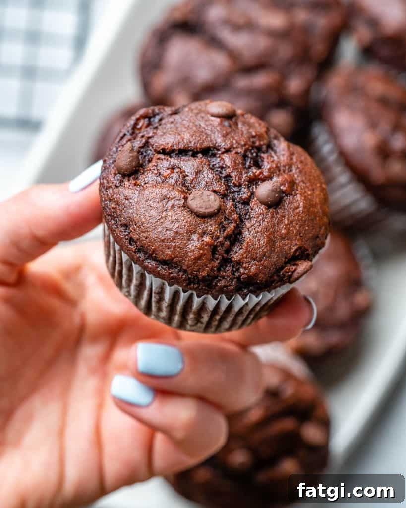 Hand holding chocolate peanut butter banana muffin with more muffins in background