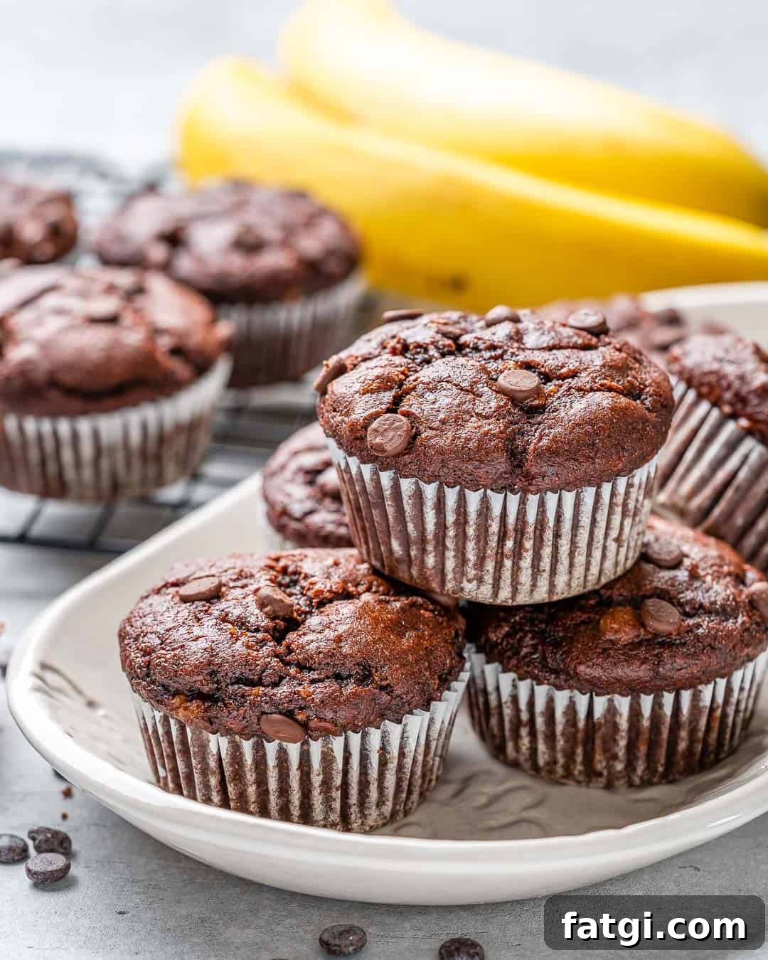White tray of healthy chocolate peanut butter banana muffins with bananas in background