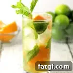 one orange mojito in a clear glass with a bowl of limes and oranges in the background