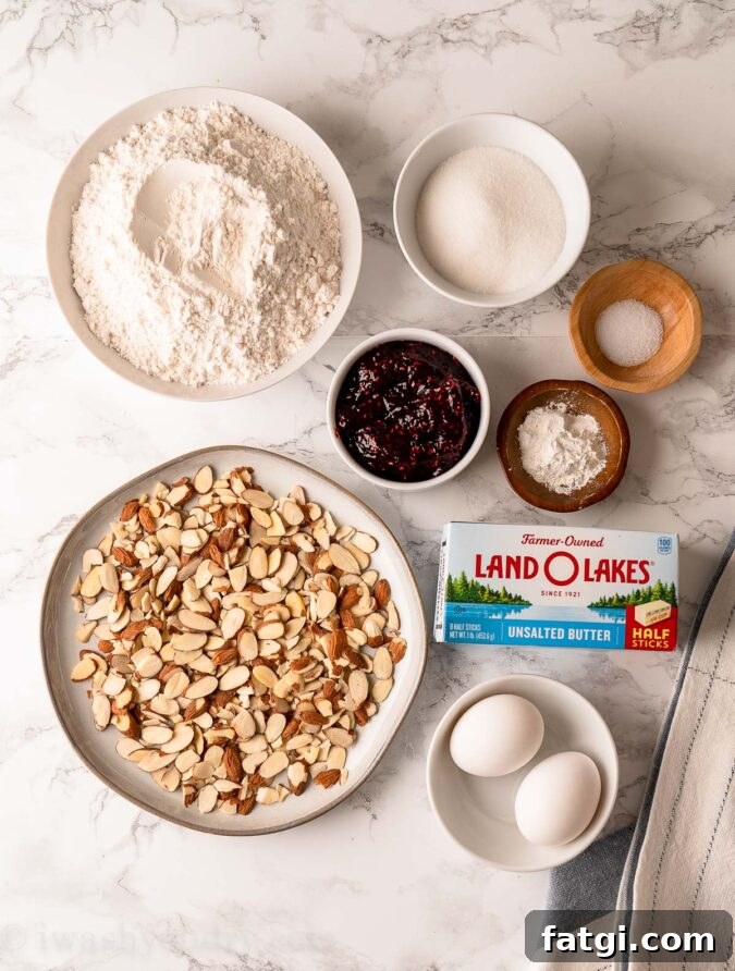 ingredients for thumbprint cookies on white table with almonds and raspberry jam