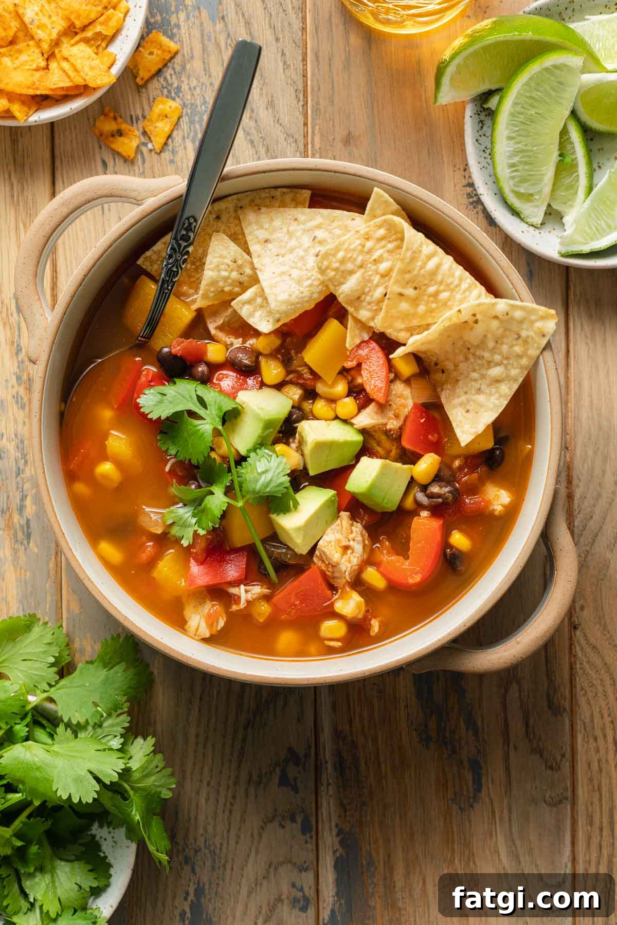 Overhead view of chicken fajita soup in a bowl next to cilantro and lime wedges.