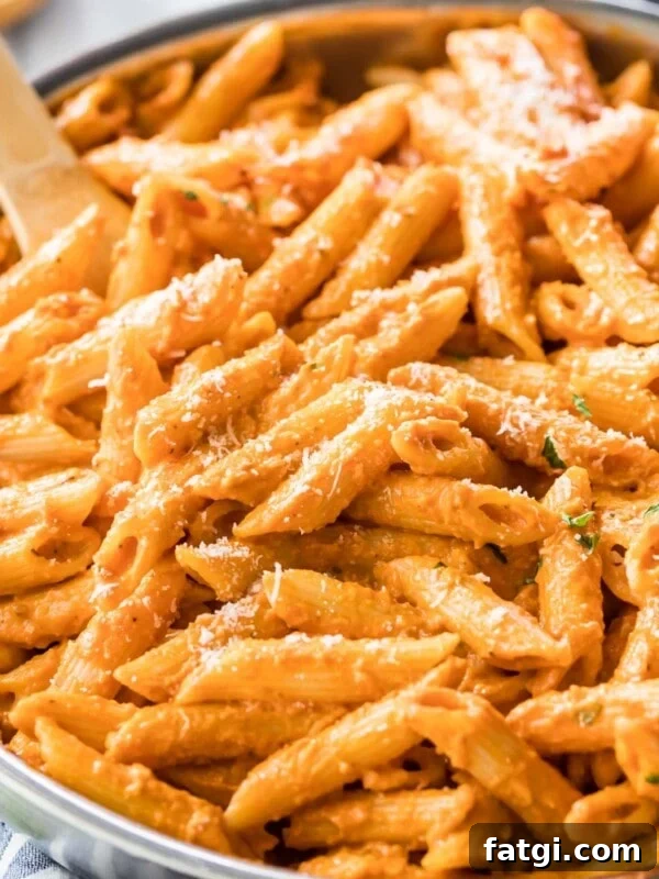 Wooden spoon resting in a large skillet of penne alla vodka topped with parmesan cheese.