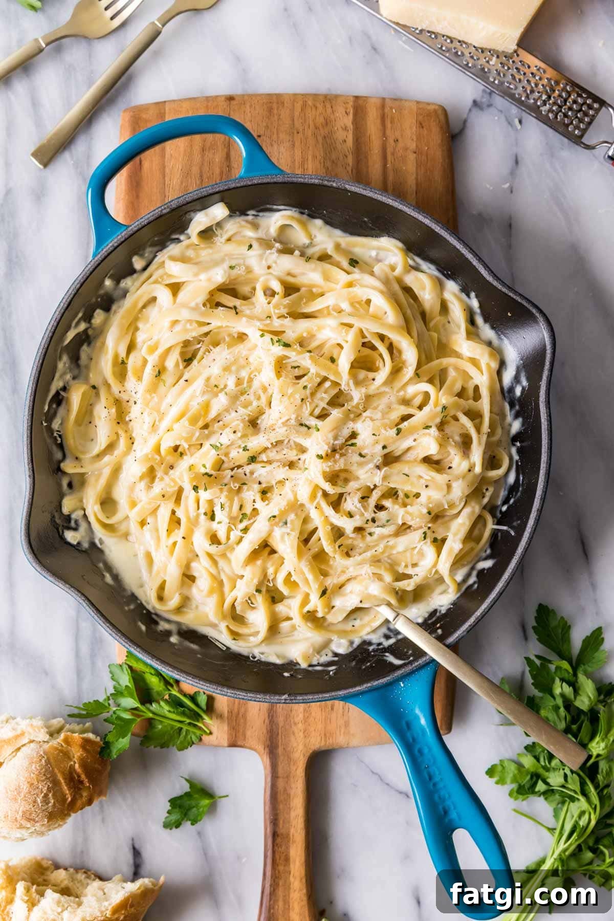 Overhead view of a skillet of fettuccine alfredo on a wood cutting board.