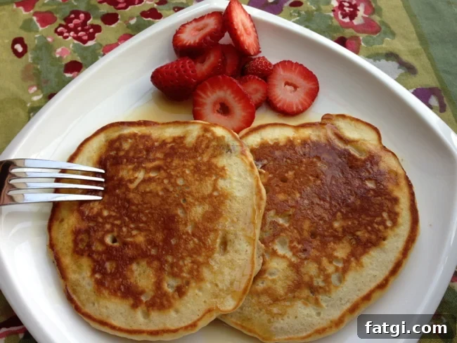 Debs Fluffy Pancake Recipe 2 A plate of perfect pancakes with syrup poured on top and fresh strawberries on the side.