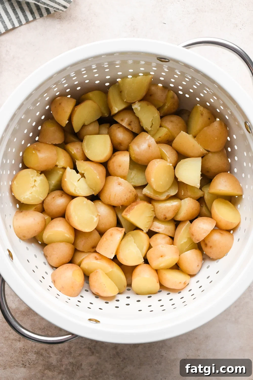 Cooked baby potatoes drained in a large white strainer.