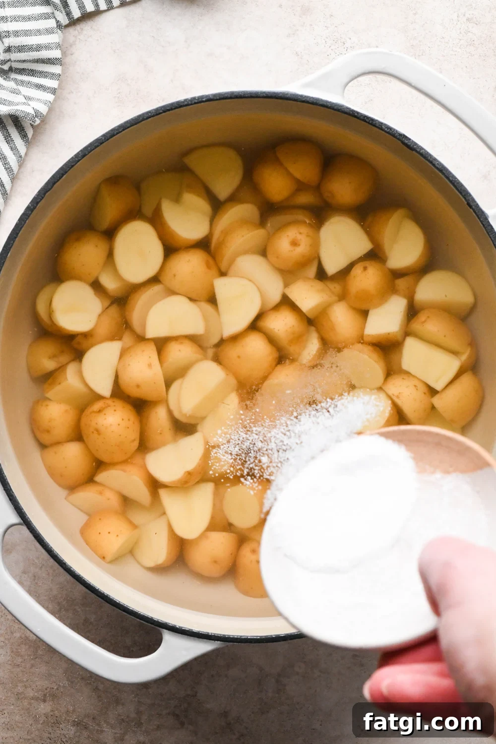 How to make Dill Pickle Potato Salad with Creamy Dill Dressing: A hand pouring kosher salt into a large pot that contains cut baby potatoes covered with water.