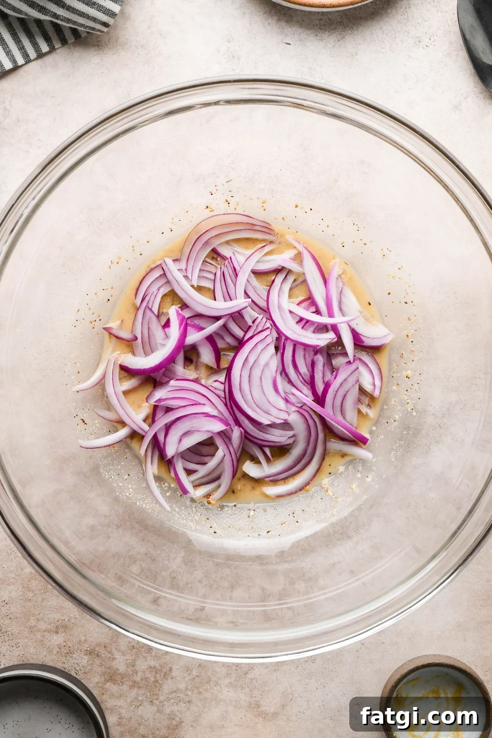Thinly sliced raw red onion added to the large glass bowl with mustard, vinegar, and pickle brine mixture.