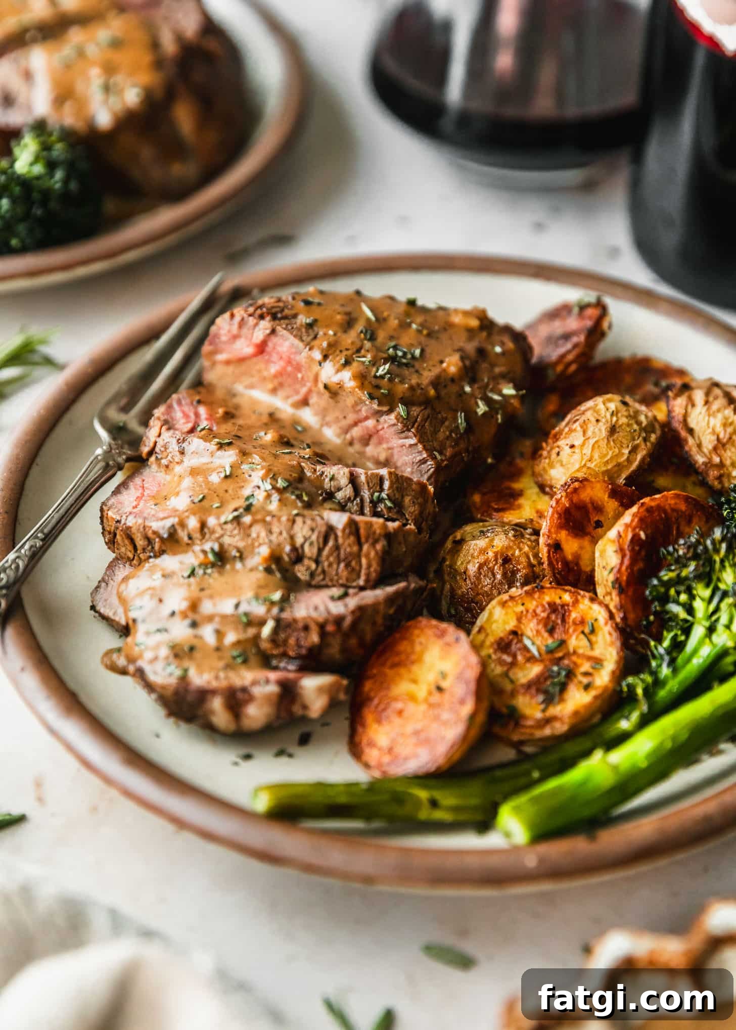 Reverse-Seared Filet Mignon with Creamy Peppercorn Sauce 7 Reverse sear filet mignon with peppercorn sauce, potatoes, and broccolini on a white plate next to red wine and a beige linen with a marble counter.