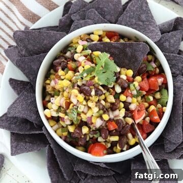 Corn and black bean salsa served in a white bowl with a blue tortilla chip.