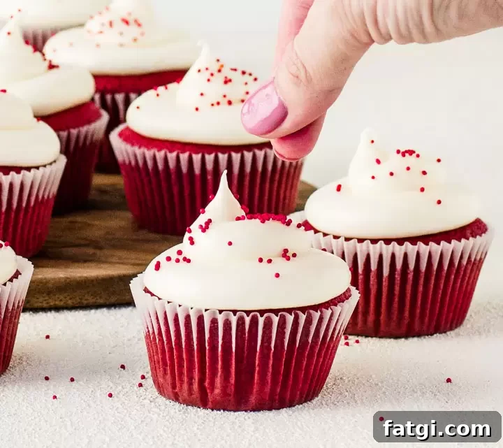 Red Velvet Cheesecake Cupcakes Recipe with Cream Cheese Swirl 2 hand sprinkling red nonpareil sprinkles on frosted cupcakes