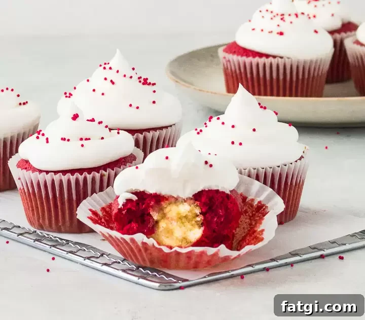Red Velvet Cheesecake Cupcakes Recipe with Cream Cheese Swirl 7 frosted red velvet cheesecake cupcakes on a wire rack with the front cupcake cut in half to show the filing