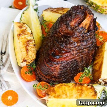 A spiral baked ham on white platter with pineapple wedges and sliced oranges
