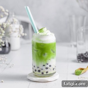 green milk tea in a glass cup with frothed milk and dusted with matcha powder.