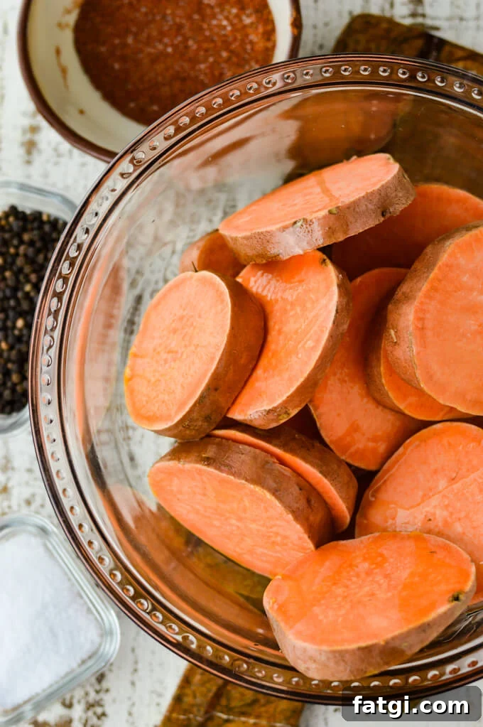 Raw sliced sweet potatoes in a clear glass bowl with a small bowl of seasoning next to it.