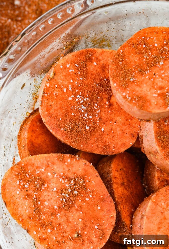 Sliced sweet potatoes in a clear glass bowl with a smoky paprika rub on them.