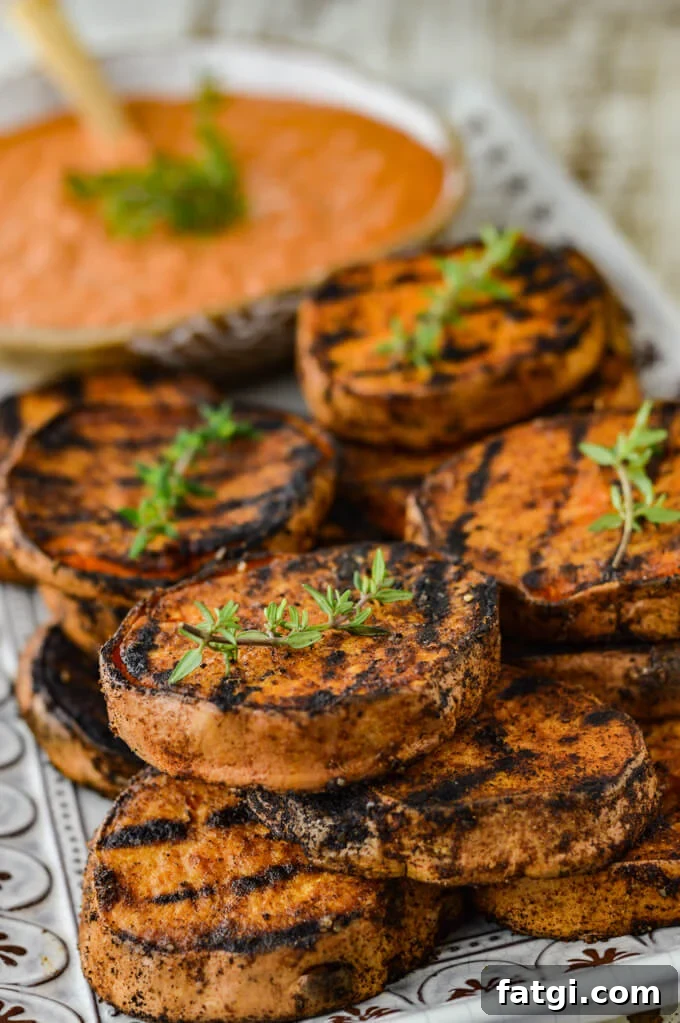 Grilled sweet potatoes on a white platter with sprigs of thyme and a bowl of dipping sauce.