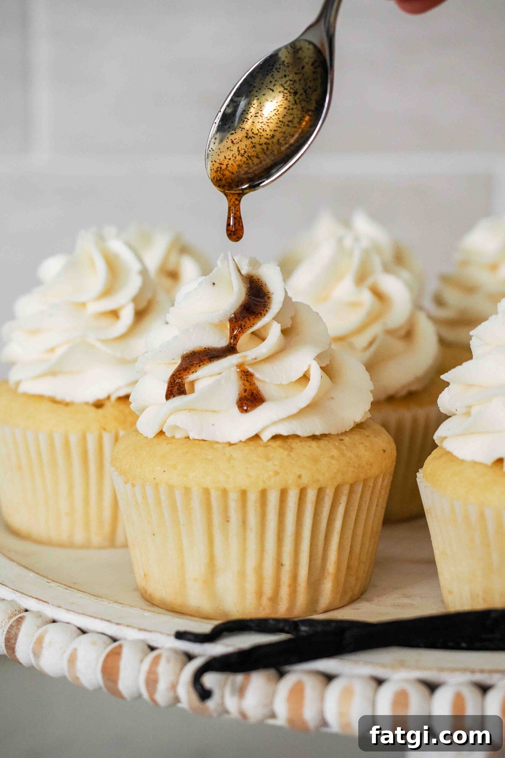 A spoon drizzles vanilla bean paste over a vanilla cupcake.