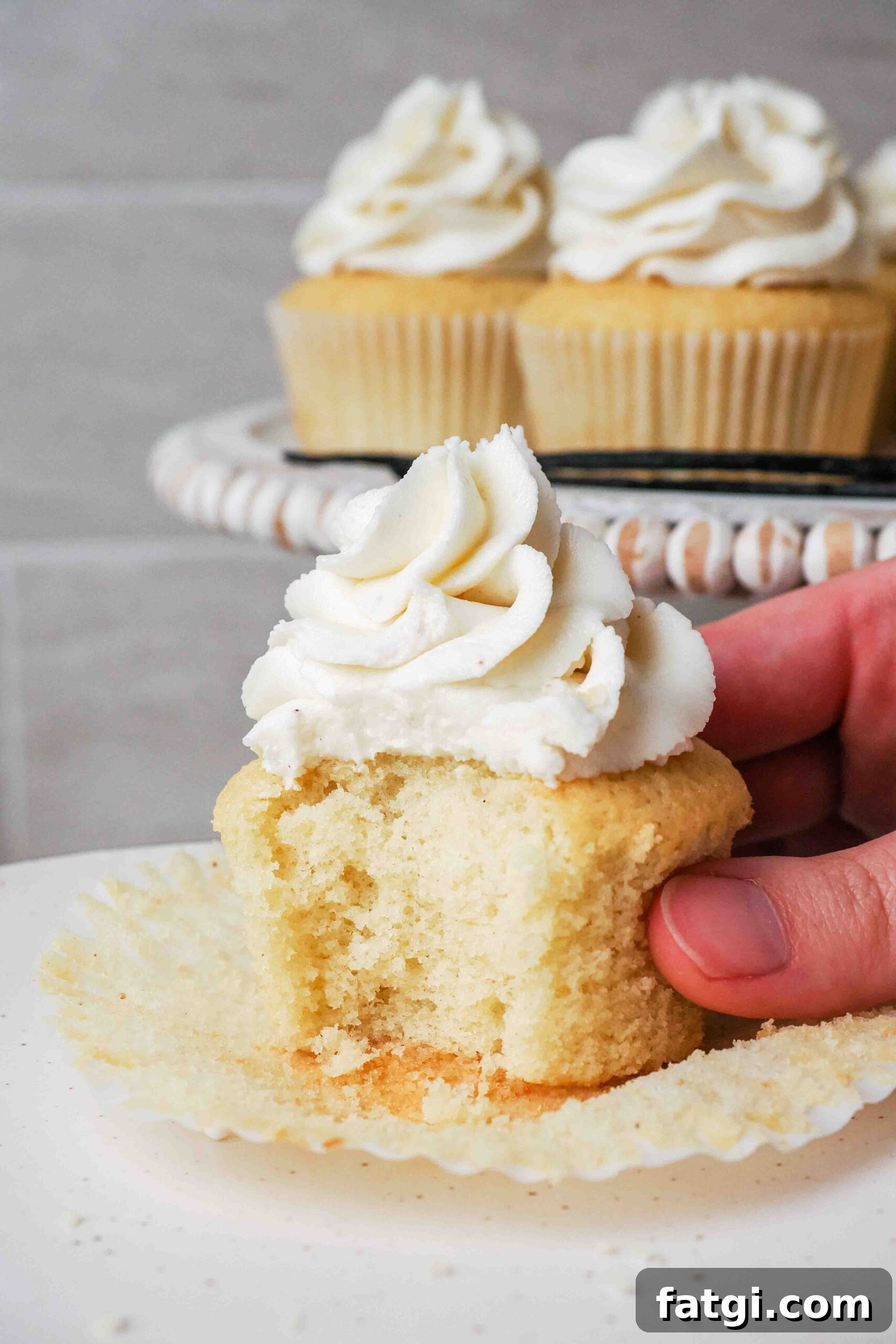 A hand holds a half-eaten vanilla bean cupcake.