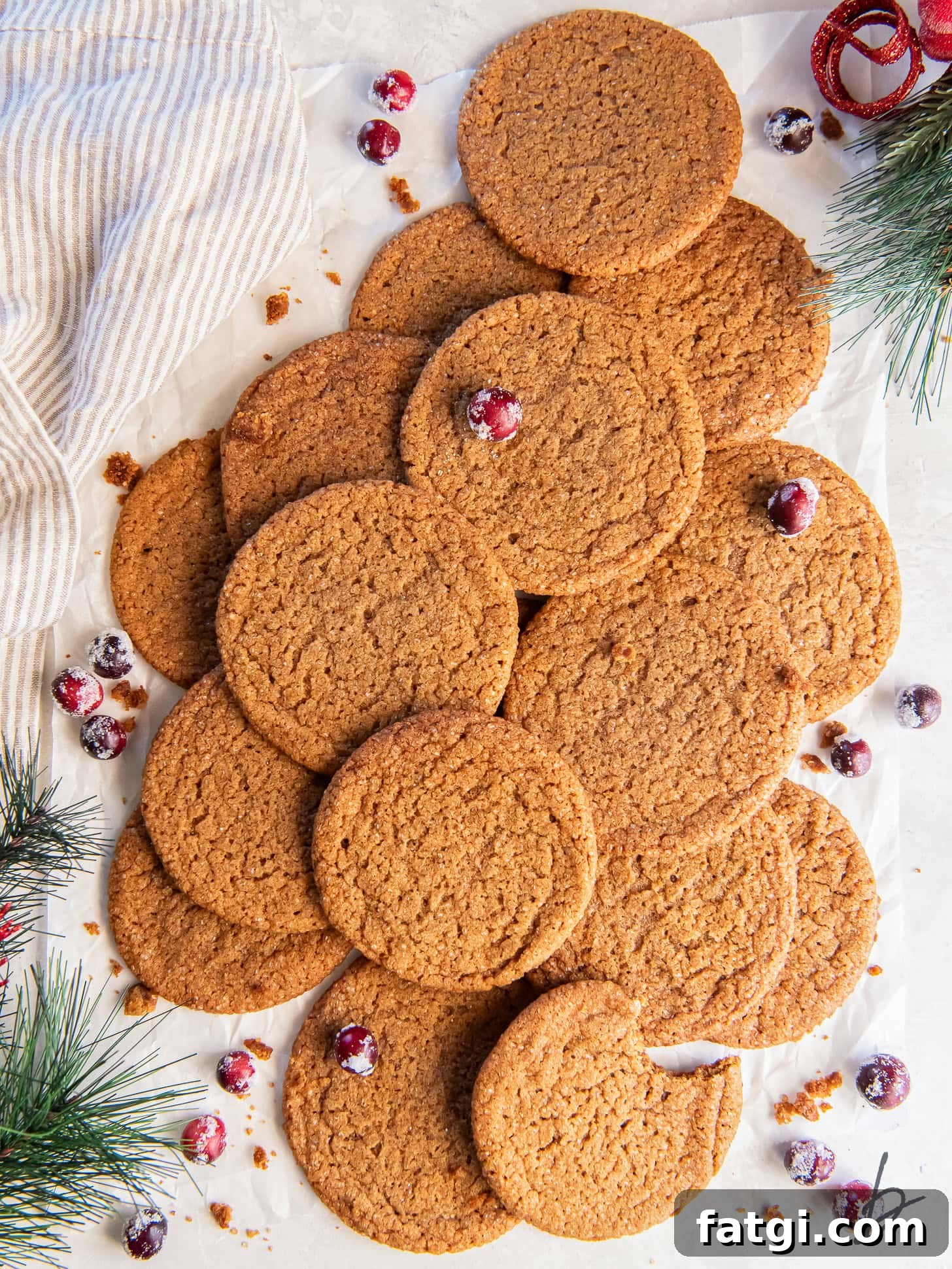 pile of gingersnap cookies on tabletop with some sugared cranberries and faux greenery.