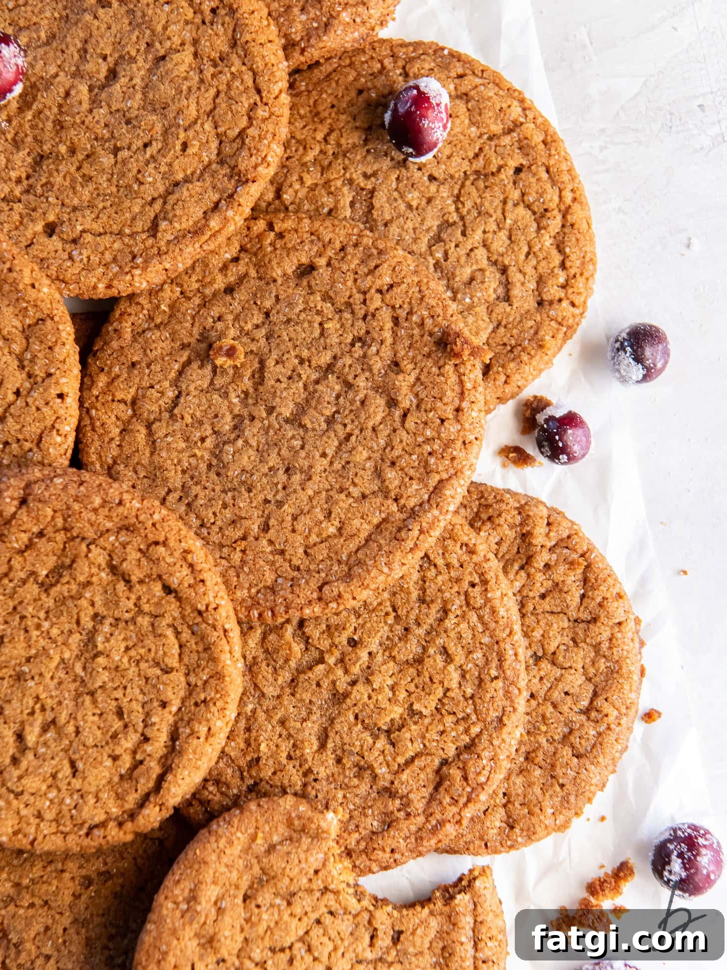 thin and crispy gingersnaps in a pile with a couple of sugared cranberries for garnish.